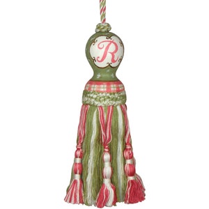 Puede incluir: Borla verde y rosa con un patrón de cuadros verde y blanco y una bola verde con una letra R rosa en ella.