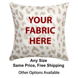 May include: Square decorative pillow with a neutral leopard print pattern. The pillow has a white background with tan spots. The text "YOUR FABRIC HERE" is in the center of the pillow in red letters.