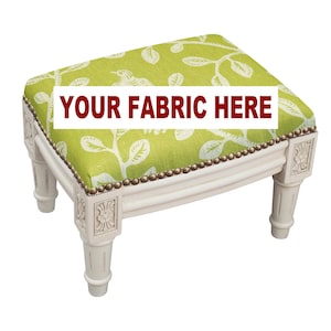 May include: A small, white, decorative footstool with a rectangular, lime green seat featuring a white leaf and bird pattern. The seat is trimmed with small, gold-colored studs. The text "YOUR FABRIC HERE" is displayed on the seat.