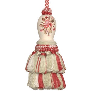 May include: A white tassel with a red and white striped band and a white ceramic top with a painted floral design.