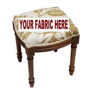 May include: A small, wooden stool with a floral patterned seat. The seat cushion features a cream background with gold-colored floral designs. The stool has four brown legs and the text "YOUR FABRIC HERE" in a red banner.