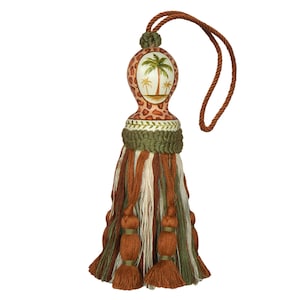 May include: Decorative tassel with a brown cord and a detailed design. The top section features a giraffe print and a painted oval with palm trees. The tassel has brown, green, and cream-colored strands.