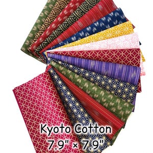 Puede incluir: Abanico de cuadrados de tela de algodón Kyoto, cada uno de 20 cm x 20 cm. Las telas presentan diversos patrones en rojo, azul, verde, amarillo y morado. Algunos tienen diseños geométricos, otros motivos florales o a rayas.