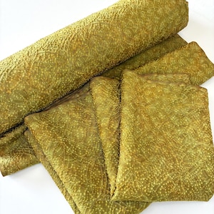 May include: A roll and several folded pieces of olive green fabric featuring a textured, raised dot pattern. The material displays a consistent, repeating geometric design across its surface, with subtle variations in colour depth and light reflection.