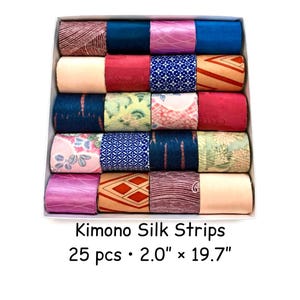 Op de afbeelding: Een doos met 25 kleurrijke kimono zijden stroken, elk 5,08 cm breed en 50,04 cm lang. De stroken zijn opgerold en in rijen gerangschikt, met een verscheidenheid aan patronen en kleuren, waaronder roze, blauw en rood.