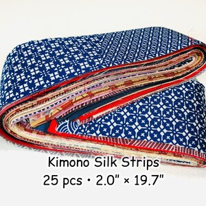 Puede incluir: Una pila de 25 tiras de tela dobladas etiquetadas como Kimono Silk Strips 25 pcs 5,08 cm x 50,04 cm. Las tiras presentan varios patrones, incluyendo diseños geométricos en azul y blanco, acentos rojos y motivos florales con bordes visibles.