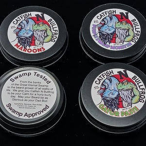 May include: Four black metal tins with lids. Each tin has a colorful label with a cartoon catfish and bullfrog. The labels read "Catfish N Bullfrog" and include the names "Maroons", "Swamp Monster", "Gator Paste", and "Swamp Tested".