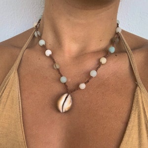 Peut inclure: Un collier en cordon marron avec des perles vert clair et blanches et un pendentif en forme de coquille.