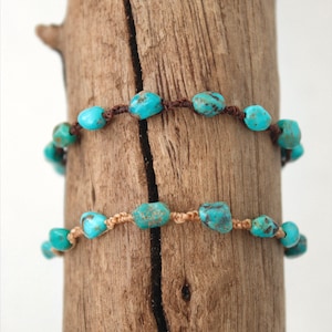 Puede incluir: Dos pulseras de piedras turquesa con cordón marrón y beige. Las pulseras están envueltas alrededor de un trozo de madera flotante.