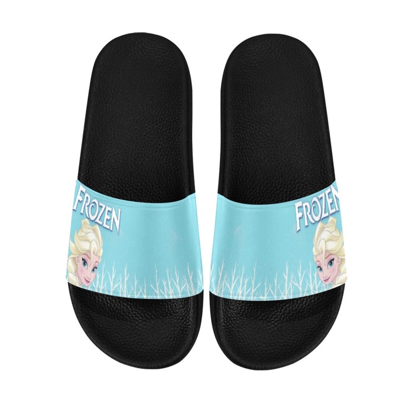 May include: A pair of black slide sandals with a blue and white design featuring the word "FROZEN" and an image of Elsa from the Disney movie Frozen.