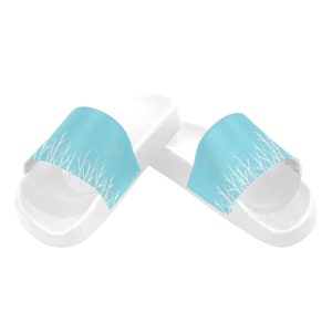 May include: A pair of white slide sandals with a light blue strap featuring a white branch pattern.