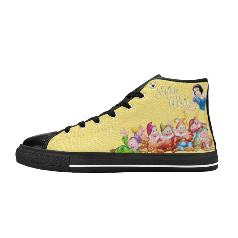 K&ouml;nnte beinhalten: Hohe Canvas-Sneaker mit gelbem Hintergrund und schwarzer Zehenkappe. Das Design zeigt Schneewittchen und die sieben Zwerge. Der Text "Snow White" ist in einer Schreibschrift auf die Seite des Schuhs geschrieben. Die Schn&uuml;rsenkel und die Sohle sind schwarz.