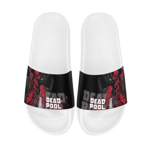 Può includere: Un paio di ciabatte bianche con una grafica di Deadpool nera e rossa e il testo "DEADPOOL" sulla fascia.
