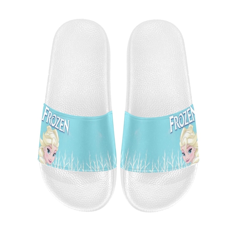 May include: A pair of white slip-on sandals with a blue and white Frozen design. The sandals feature a picture of Elsa from the movie Frozen and the word "Frozen" on each sandal.