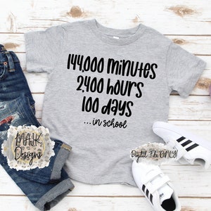 May include: A gray t-shirt with black text that reads "144,000 minutes 2,400 hours 100 days... in school". The shirt is on a wooden surface with a pair of white sneakers with black stripes and a small potted plant.