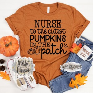 May include: A brown t-shirt with the text "NURSE to the cutest PUMPKINS IN THE patch" in black. The shirt is laying on a white surface with a pumpkin, fall leaves, and a pair of white sneakers.