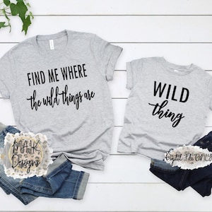 May include: Two grey t-shirts with black text. The larger shirt says "Find me where the wild things are". The smaller shirt says "Wild thing".