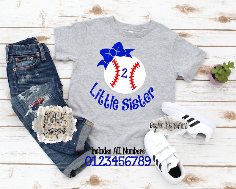 Puede incluir: Una camiseta gris con una pelota de b&eacute;isbol blanca con un lazo azul en la parte superior. La pelota de b&eacute;isbol tiene un n&uacute;mero 2 rojo en ella. El texto "Little Sister" est&aacute; escrito debajo de la pelota de b&eacute;isbol. El texto "Includes All Numbers 0123456789" est&aacute; escrito debajo de la camiseta.