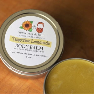 Könnte beinhalten: Eine silberne Dose mit einem weißen Etikett, auf dem steht "& SUNFLOWER & RED - a small family business - Tangerine Lemonade BODY BALM ALL NATURAL INGREDIENTS HANDMADE IN SMALL BATCHES 8 oz". Die Dose enthält einen gelben Körperbalsam.