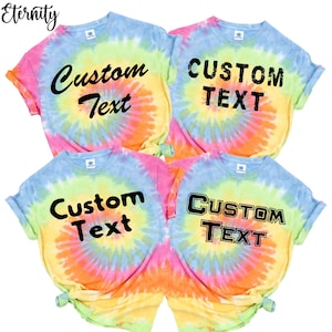May include: Four tie-dye t-shirts in a rainbow of colors, including pink, yellow, blue, and orange. Each shirt has the words "Custom Text" printed in black. The shirts are short-sleeved.