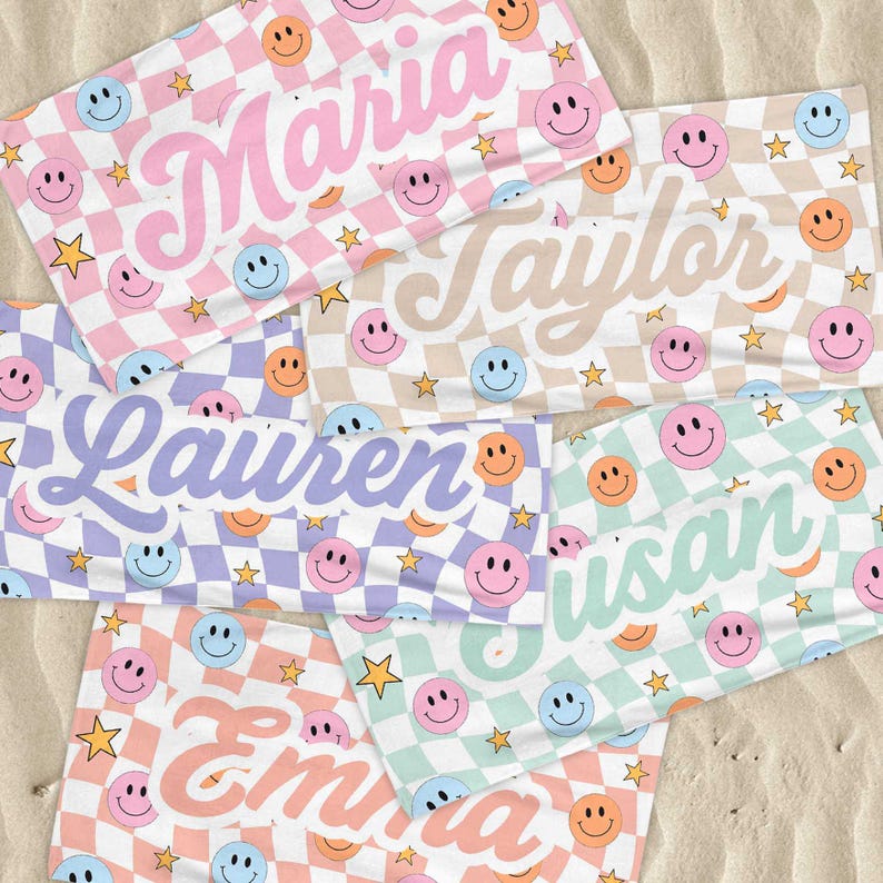 K&ouml;nnte beinhalten: Mehrere personalisierte Strandt&uuml;cher mit Namen wie "Maria" und "Taylor" werden gezeigt. Jedes Handtuch hat ein Schachbrettmuster mit Smiley-Gesichtern und Sternen in verschiedenen Pastellfarben, darunter Rosa, Blau und Gr&uuml;n.