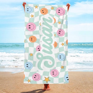 K&ouml;nnte beinhalten: Ein Strandtuch mit einem wei&szlig;-hellgr&uuml;nen Schachbrettmuster, verziert mit rosa, orangefarbenen und blauen Smileys sowie gelben Sternen. Der Name "Susan" ist in Schreibschrift geschrieben.