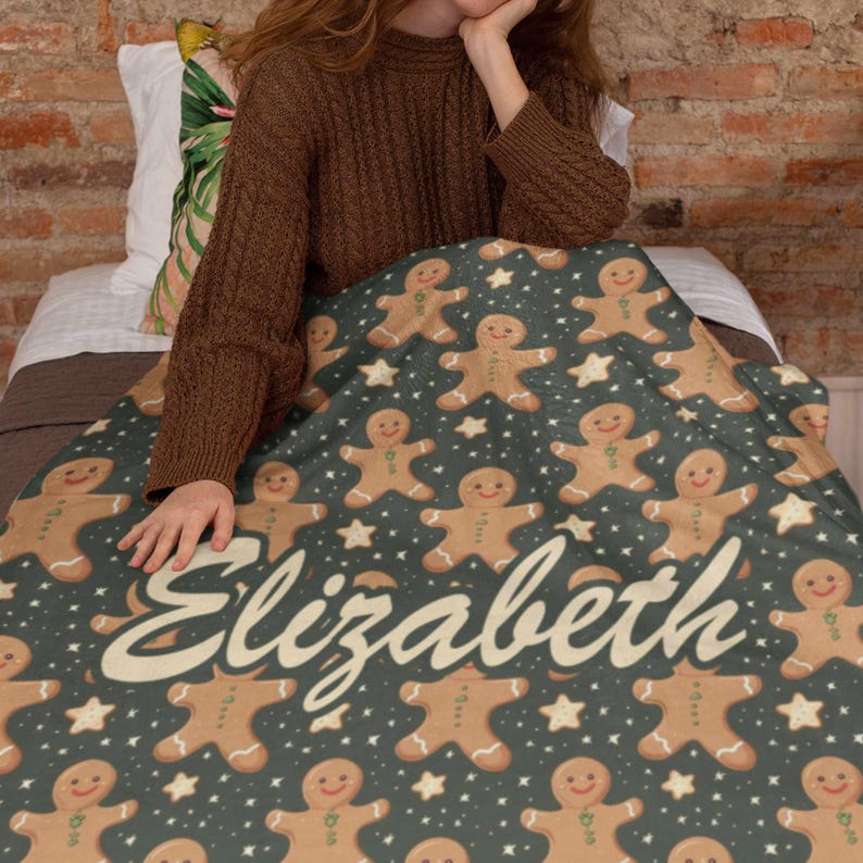 May include: A dark teal blanket featuring a pattern of gingerbread men and white stars. The blanket has the name "Elizabeth" in a cursive font. The blanket is made of a soft material and is perfect for the holiday season.