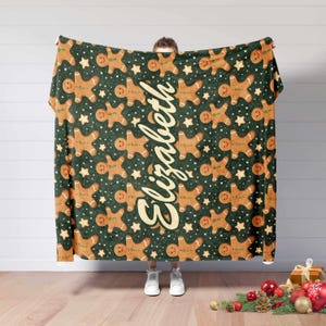 May include: A green blanket with a repeating pattern of gingerbread men and stars. The name "Elizabeth" is written vertically in a cursive font. The blanket is a festive holiday item.