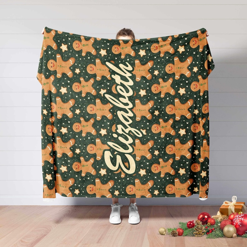 May include: A green blanket with a repeating pattern of gingerbread men and stars. The name "Elizabeth" is written vertically in a cursive font. The blanket is a festive holiday item.