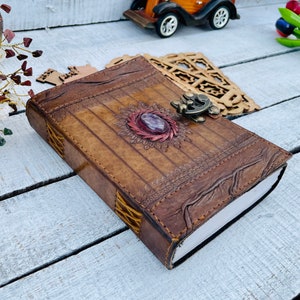 May include: A brown leather journal with a decorative metal clasp and a purple gemstone. The journal has a distressed look and is closed.