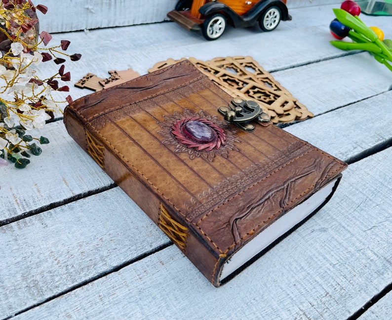 May include: A brown leather journal with a decorative metal clasp and a purple gemstone. The journal has a distressed look and is closed.