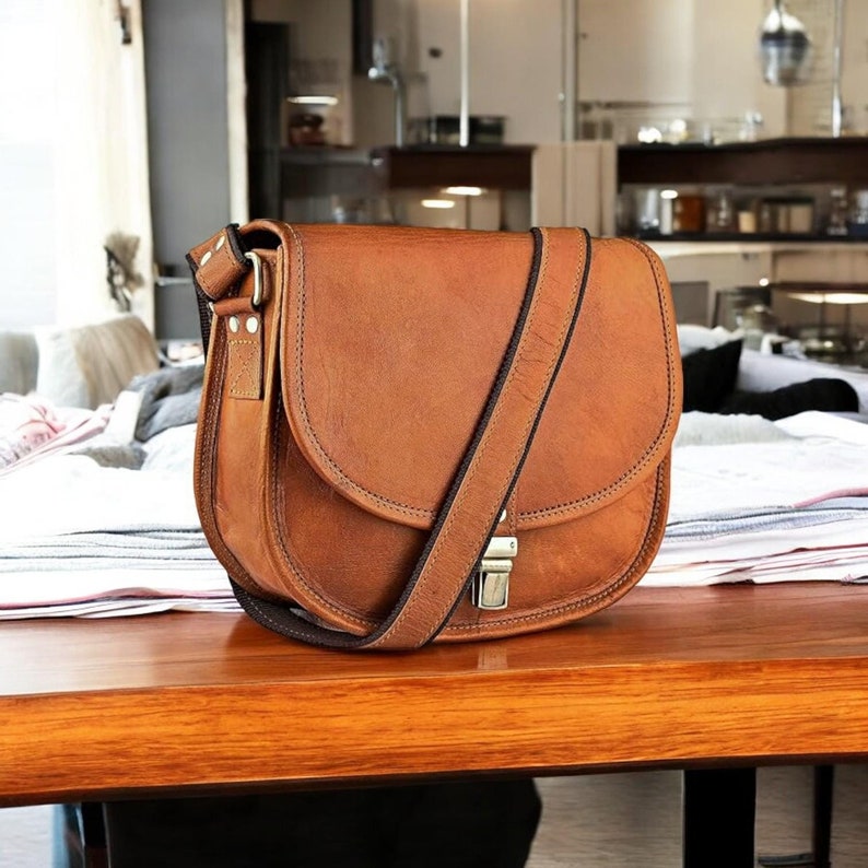 Pu&ograve; includere: Una borsa a tracolla in pelle marrone con chiusura a lembo e fibbia argentata. La borsa ha una lunga tracolla regolabile.