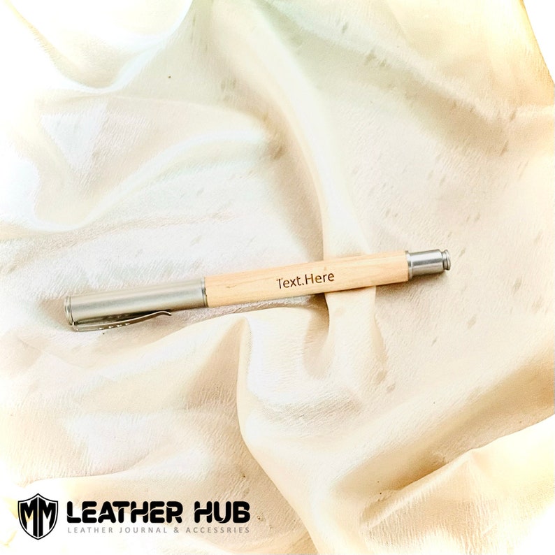 May include: A wooden pen with a silver clip and a silver end cap. The pen is engraved with the text "Text.Here".