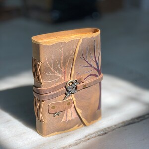 May include: A brown leather journal with a tree design and a key-shaped closure. The journal has a rustic look and is perfect for writing down thoughts and ideas.