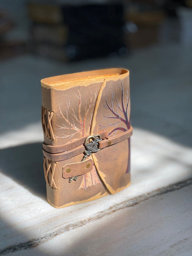 May include: A brown leather journal with a tree design and a key-shaped closure. The journal has a rustic look and is perfect for writing down thoughts and ideas.
