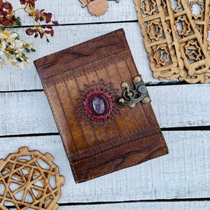 May include: A brown leather journal with a decorative floral design and a purple gemstone in the center. The journal has a metal clasp and is closed.