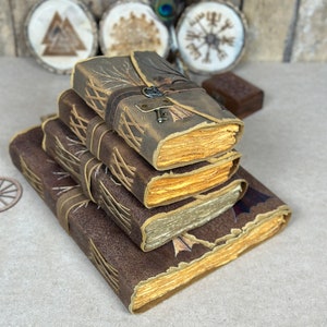 May include: A stack of four leather-bound journals with decorative stitching and aged paper. The top journal has a tree branch design and a metal keyhole.