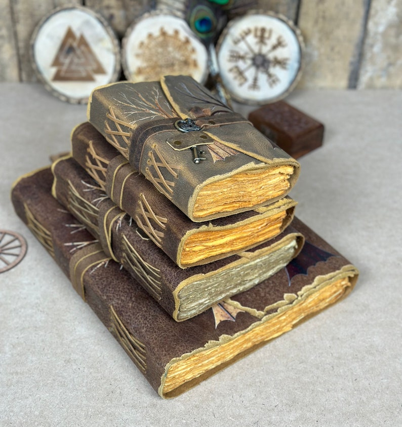 May include: A stack of four leather-bound journals with decorative stitching and aged paper. The top journal has a tree branch design and a metal keyhole.