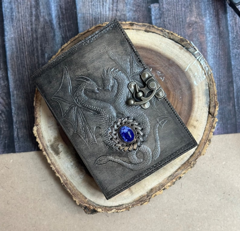 May include: A dark gray leather journal with a tooled design of two intertwined dragons and a blue gemstone clasp.