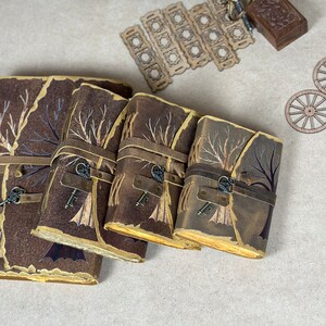 May include: Four brown leather journals with a tree design and a key charm. The journals are stacked on top of each other, with the largest journal on the bottom and the smallest journal on top.