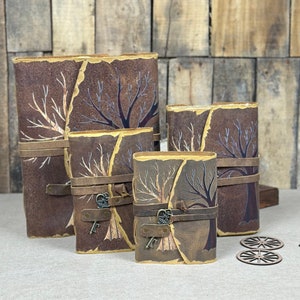 May include: Four leather-bound journals with tree designs and keyhole accents. The journals are arranged in a size progression, with the largest journal on the left and the smallest on the right.