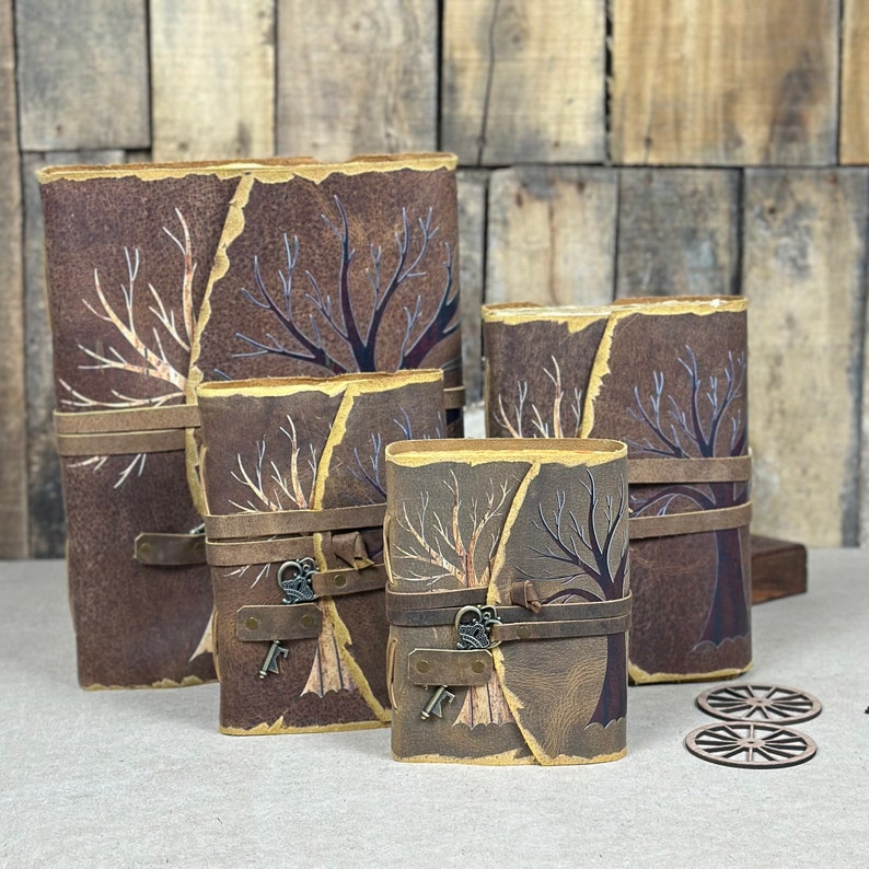 May include: Four leather-bound journals with tree designs and keyhole accents. The journals are arranged in a size progression, with the largest journal on the left and the smallest on the right.