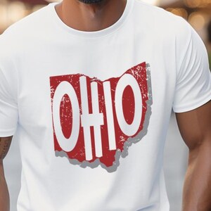 May include: White t-shirt featuring a distressed red outline of the state of Ohio with the word "OHIO" in white block letters. The shirt is a crew neck style and appears to be made of a soft material.