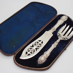 May include: A silver fish serving set, including a knife and fork, displayed in a blue velvet-lined case. The knife features an ornate, openwork design. The set is likely vintage or antique.