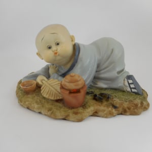 Asian Baby Figurine with feather blowing on teapot CIRCA 1980s