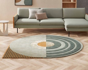 May include: A light green sectional sofa with two cushions sits in front of a light beige wall with two framed abstract art prints. A round, multi-coloured rug with a geometric design is on the floor in front of the sofa.