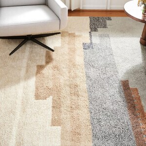 May include: A rectangular rug with a geometric pattern in cream, tan, grey, and brown vertical stripes. A modern rug suitable for a living room or bedroom, adding a touch of style.