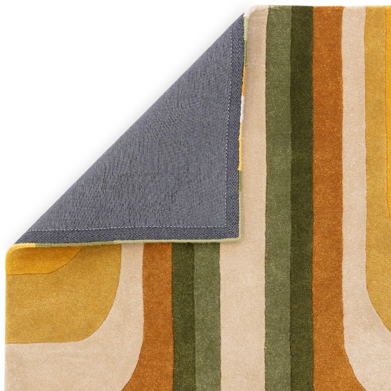May include: A colorful rug with a retro design. The rug features vertical stripes in shades of yellow, green, beige, and brown. A corner of the rug is lifted, revealing a gray backing with a green border. The rug has a soft, textured appearance.