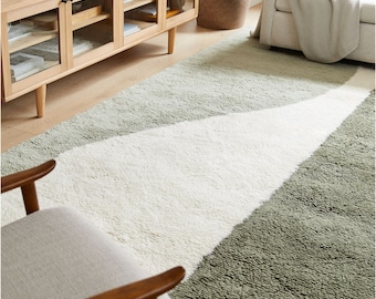 May include: A fluffy, green and white area rug with a geometric design. The rug is in a living room setting with a wooden cabinet and a white sofa.