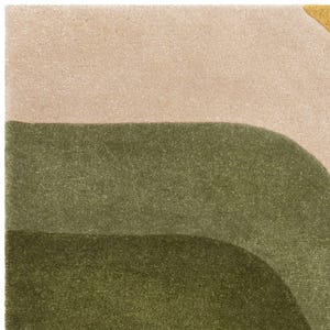 May include: A close-up of a rug with a geometric design. The rug features a beige top section, with two curved olive green sections below. A small section of yellow is visible in the upper right corner. The rug has a soft, textured appearance.